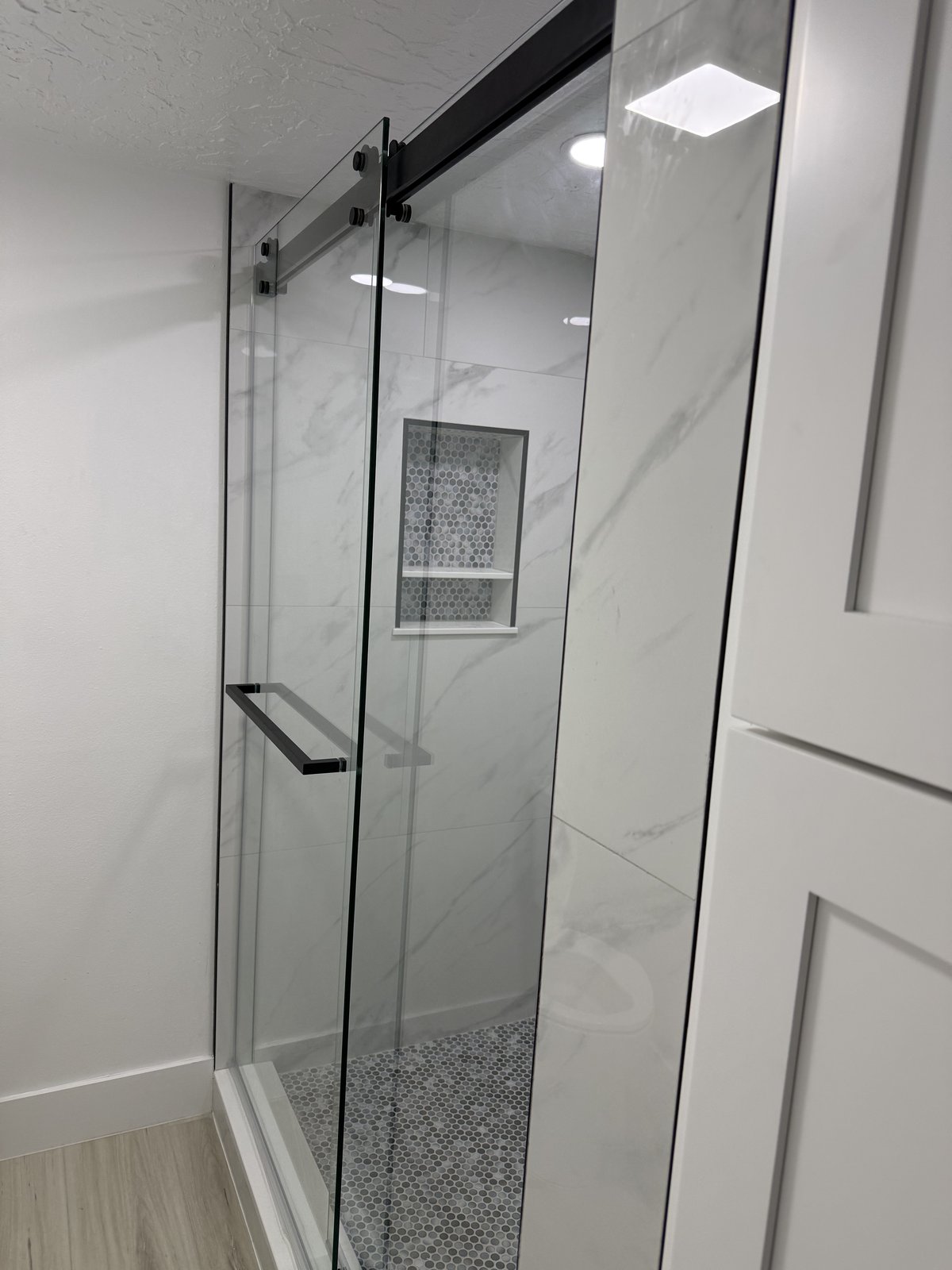 Una elegante mampara corrediza de vidrio sin marco completa esta ducha estilo mármol con piso de mosaico penny y nicho con repisa a medida.