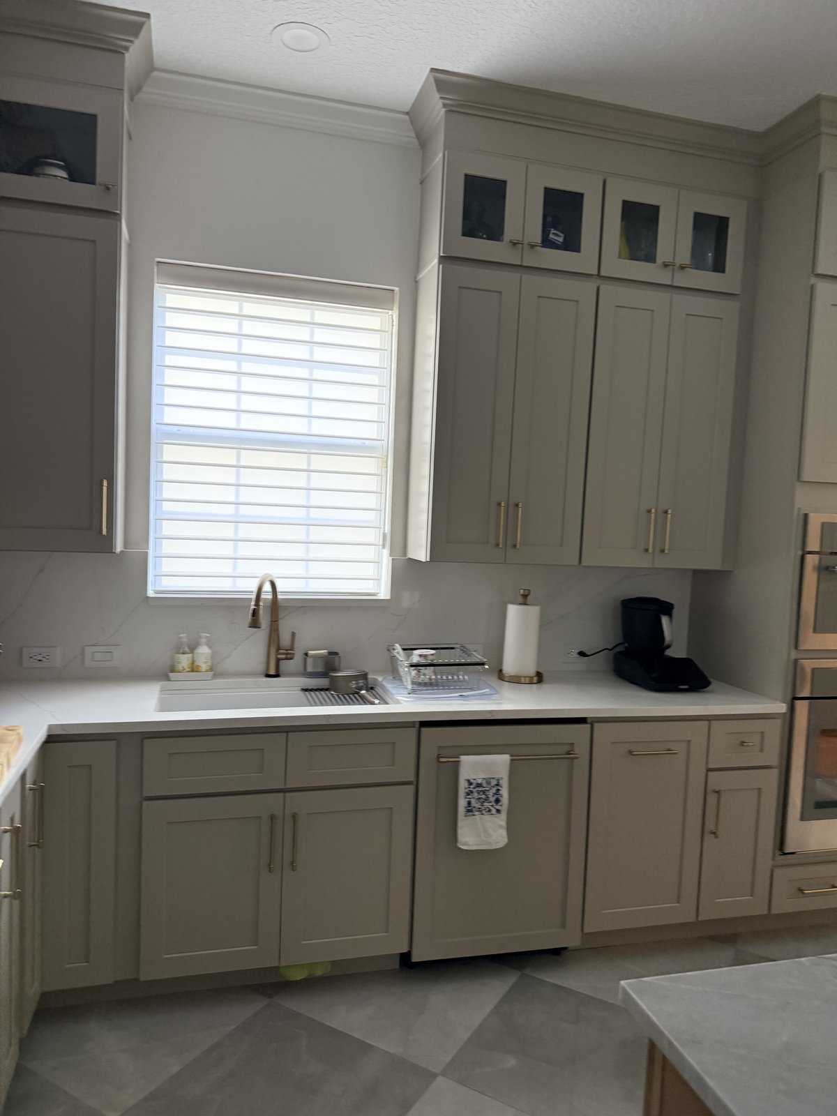 Una cocina totalmente remodelada con gabinetes estilo shaker en tono greige, herrajes dorados y elegantes superficies de cuarzo.
