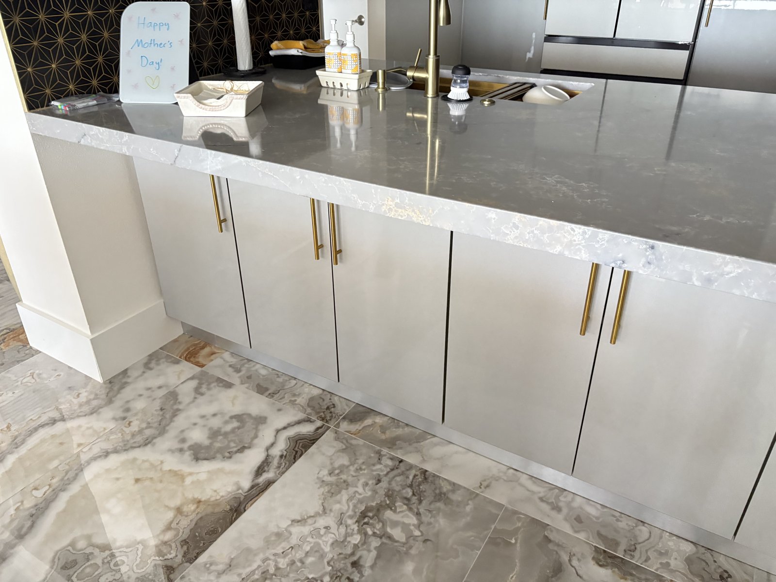 Península con encimera de cuarzo y herrajes dorados sobre un impactante piso de porcelanato tipo ónix.