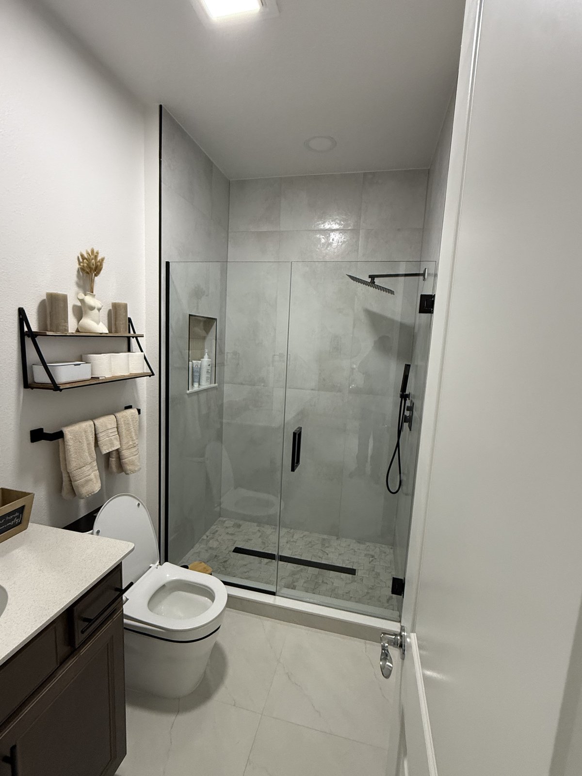 Elegante renovación de baño de visitas con ducha de vidrio sin marco, grifería negro mate y piso de mosaico de mármol.