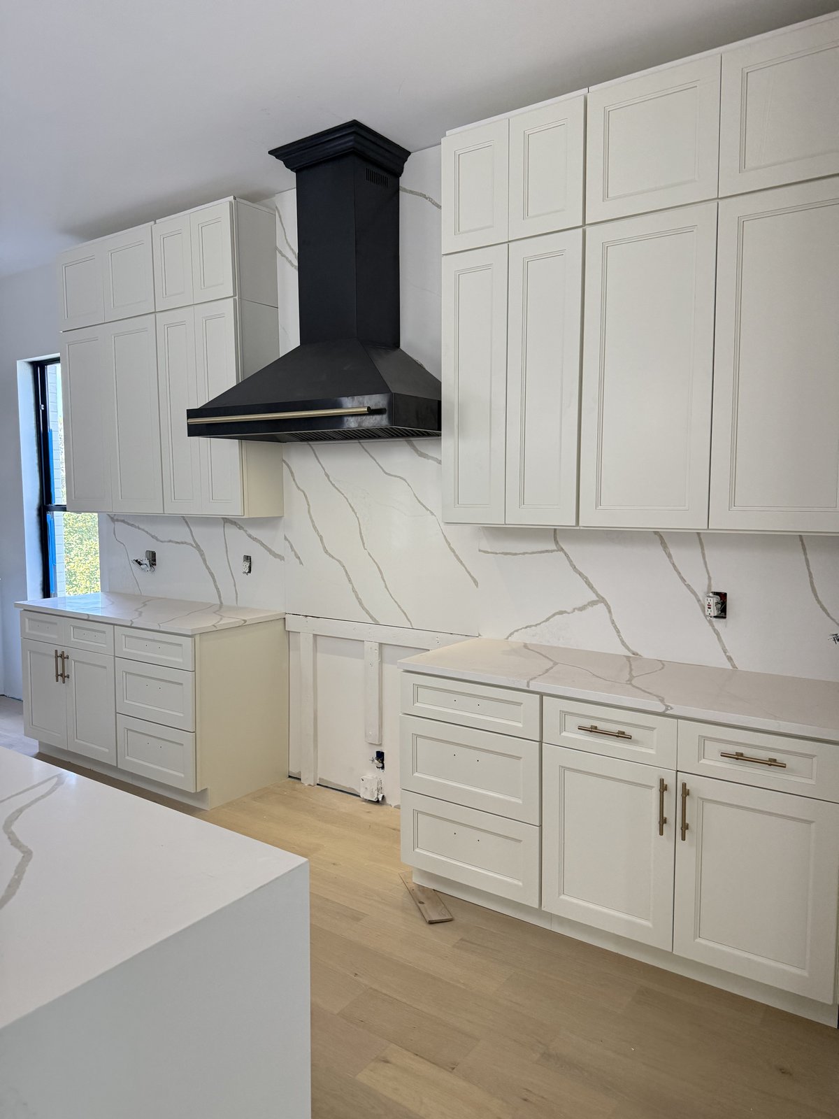 Cocina a medida tomando forma con salpicadero de cuarzo de altura completa, campana negra de diseño y pisos de roble recién instalados.