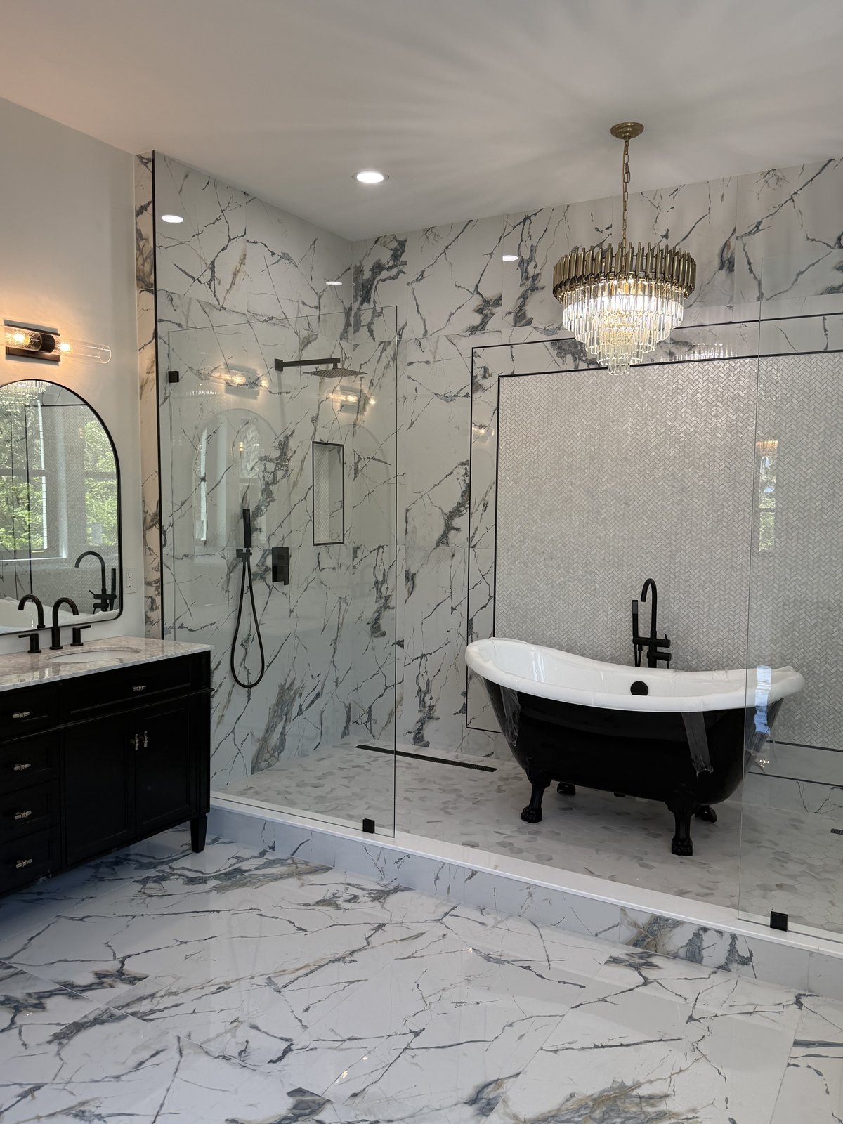 Transformación total de baño principal con porcelanato tipo mármol, tina independiente, ducha abierta de vidrio y candelabro.