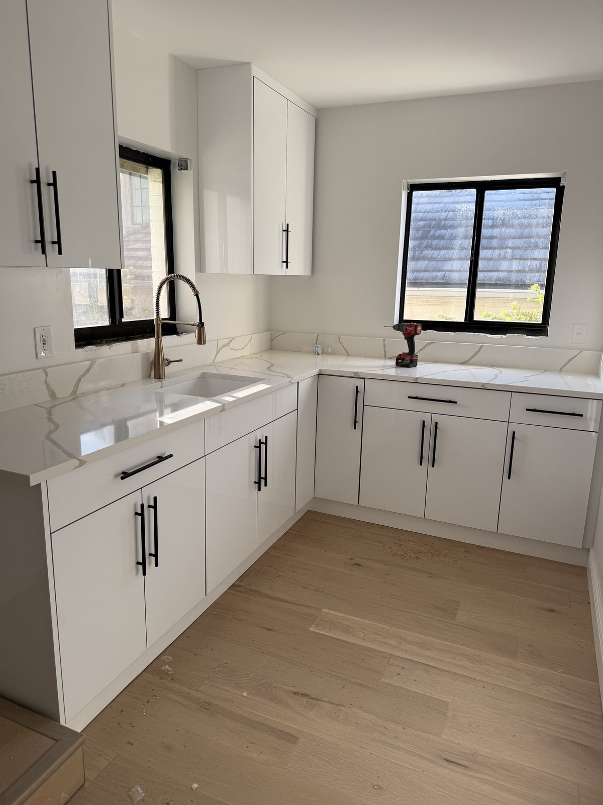 Cocina moderna y luminosa con gabinetes blancos, encimeras de cuarzo y un cálido piso de roble europeo instalado de pared a pared.