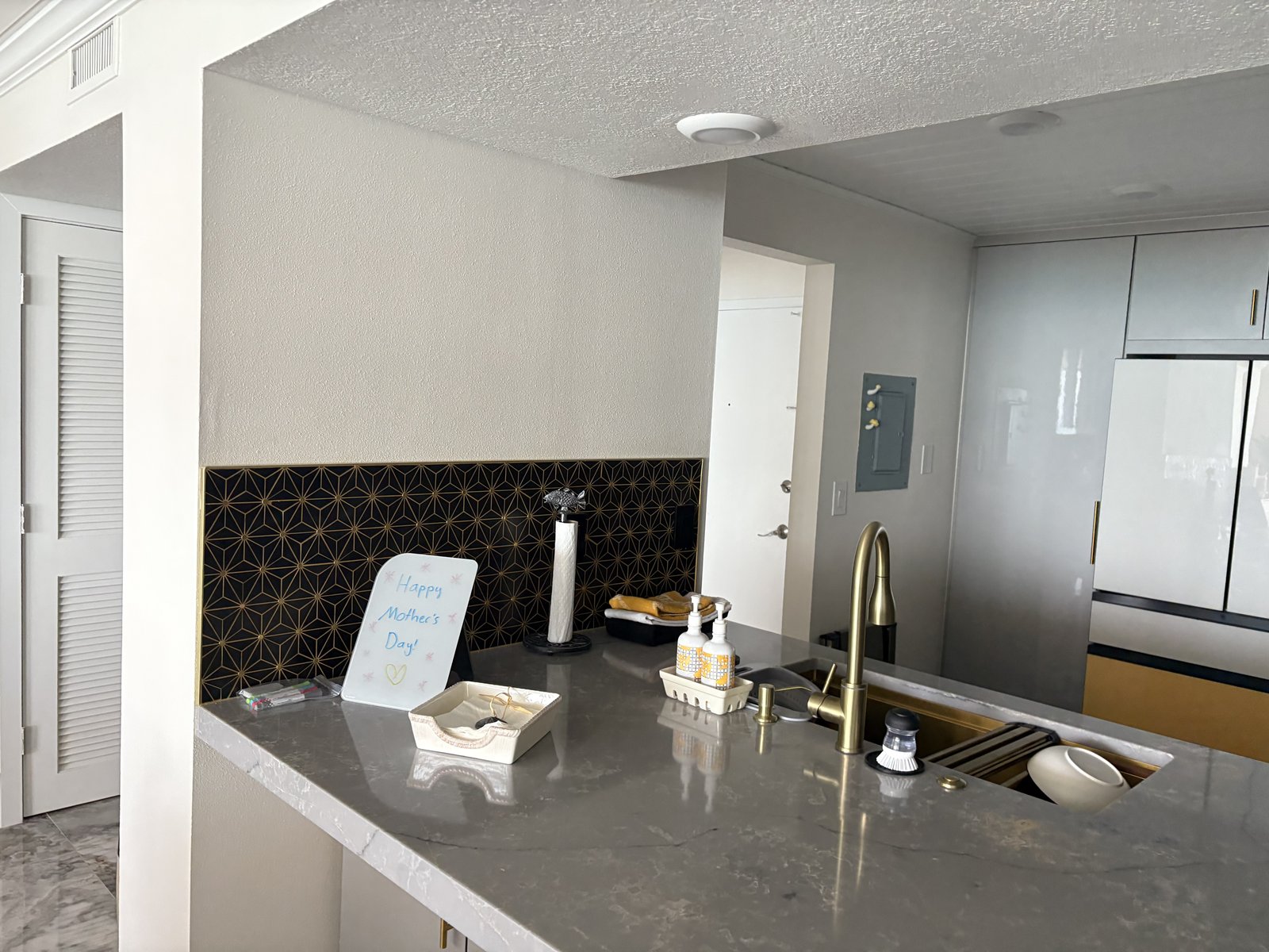 Cocina de condominio renovada con península de cuarzo gris y llamativo salpicadero geométrico en negro y dorado.