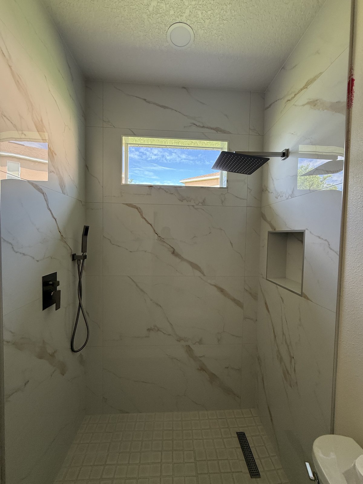 Ducha tipo spa revestida con porcelanato calacatta de gran formato, con regadera de lluvia y nicho empotrado.