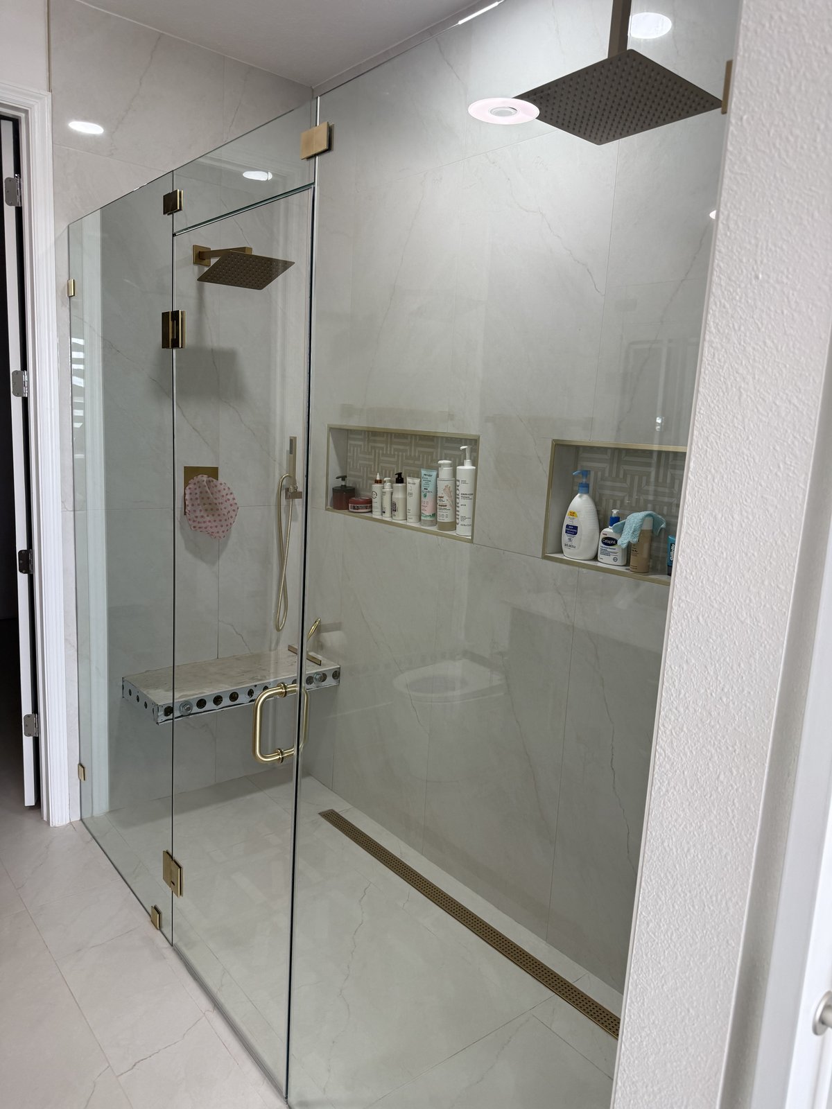Ducha a medida con azulejo tipo mármol de piso a techo, grifería en dorado cepillado y dos nichos enchapados.