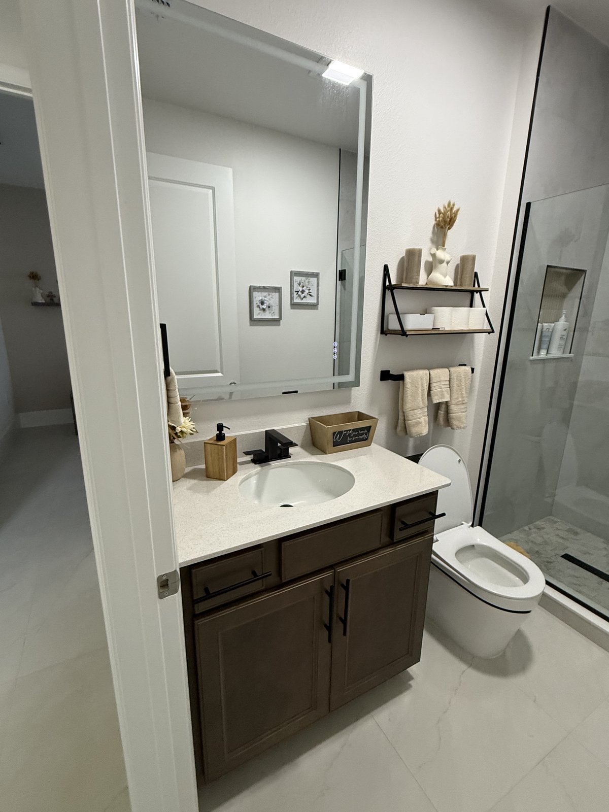 Renovación moderna de baño de visitas que combina un tocador de madera cálida con cuarzo impecable y pisos de porcelanato.