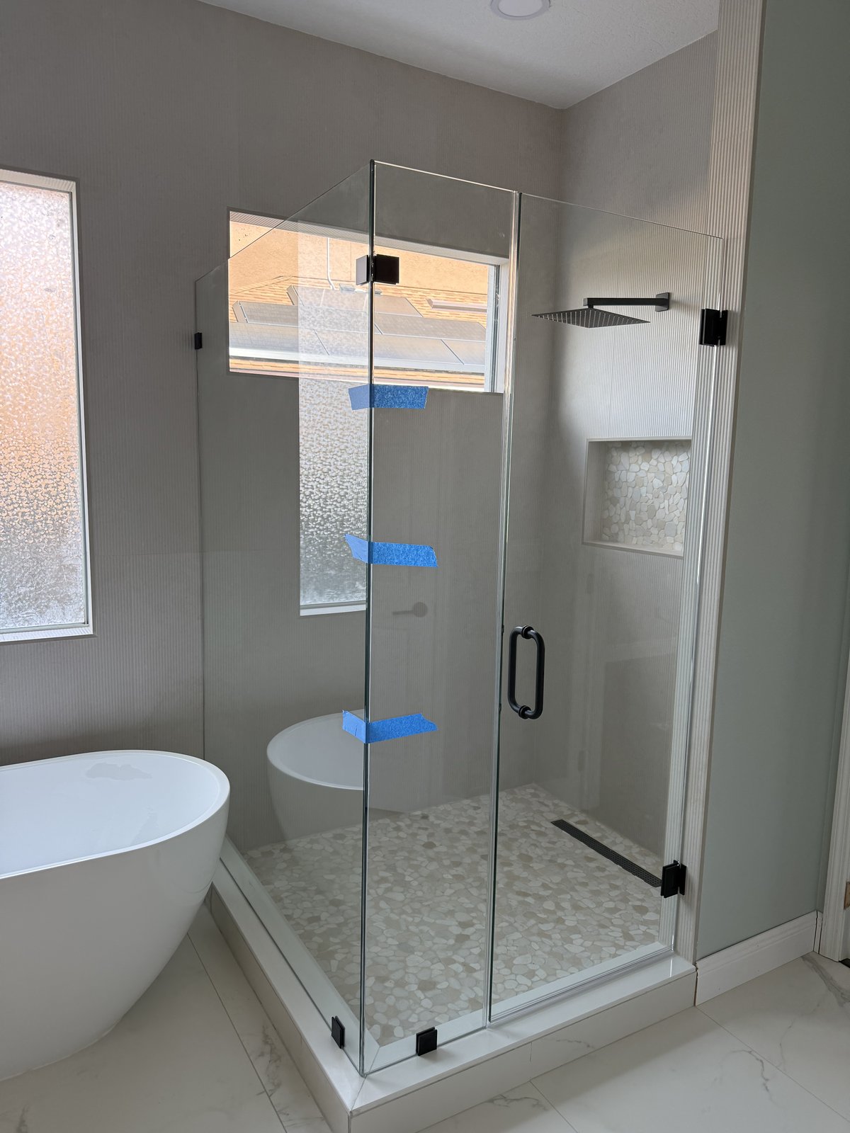 Ducha de vidrio sin marco con piso de piedra de río y regadera de lluvia, junto a una tina exenta para un verdadero refugio tipo spa.